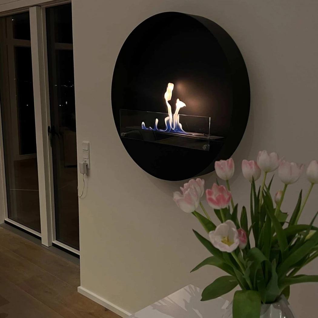 sort rund miljøvenlig biopejs med frontglas og tændte flammer på stuevæg